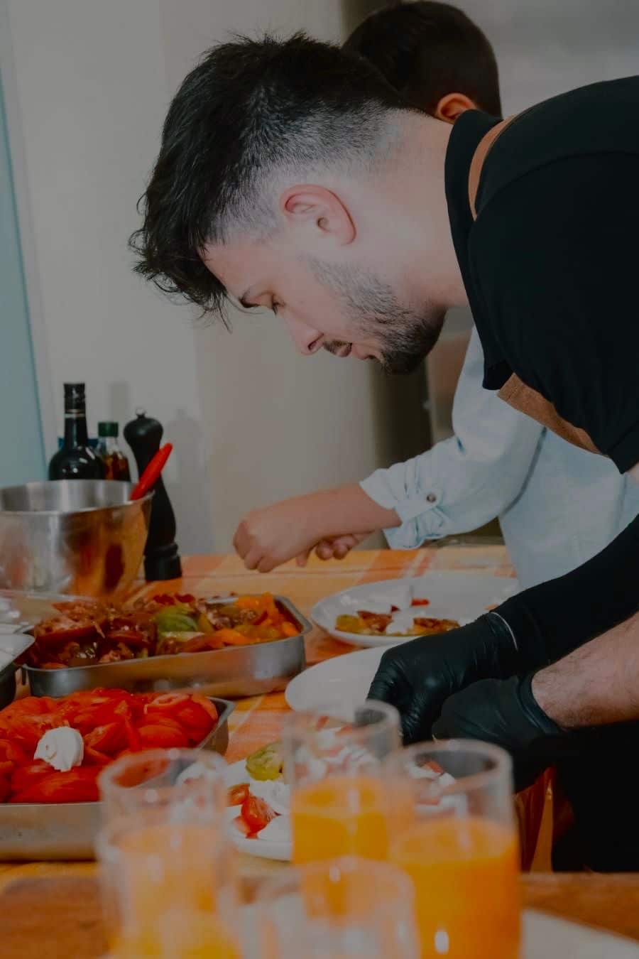 Homme en tablier préparant des plats dans une cuisine avec verres de jus à l'avant