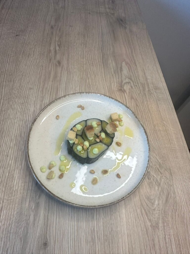 Plat gastronomique avec légumes enroulés, croûtons, pignons et crème verte sur assiette blanche
