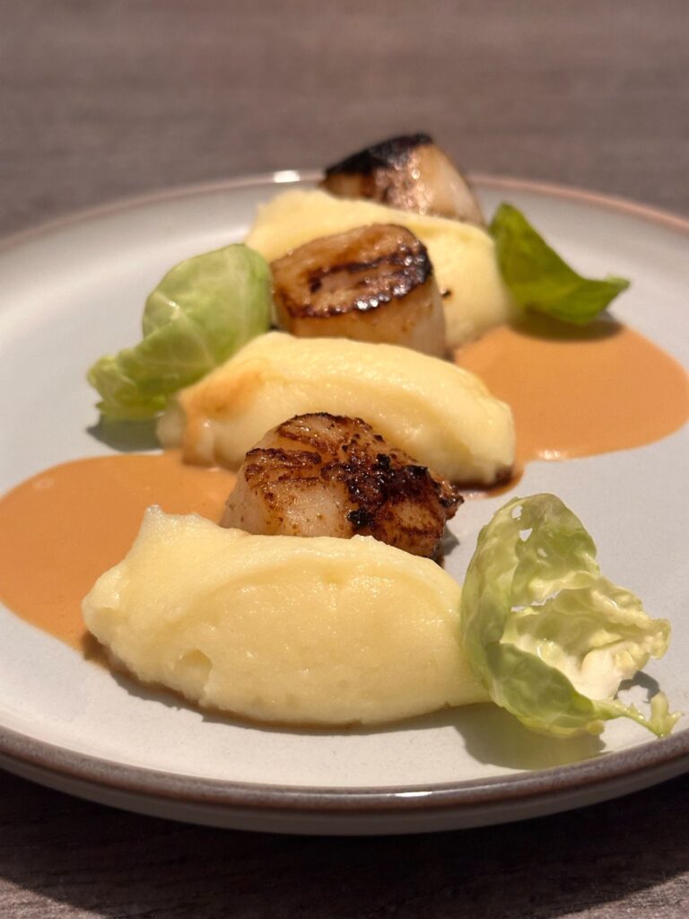 Plat gourmet avec saint-jacques poêlées, purée crémeuse et feuilles de salade verte