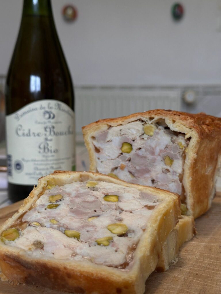 Terrine de viande aux pistaches tranchée avec bouteille de cidre bio en fond