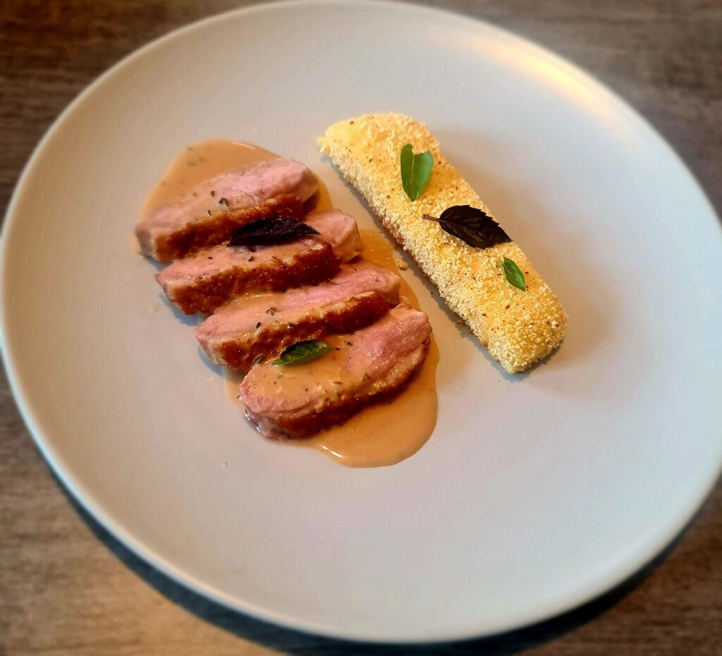Magret de canard en tranches avec sauce et accompagnement pané décoré de feuilles dans une assiette blanche