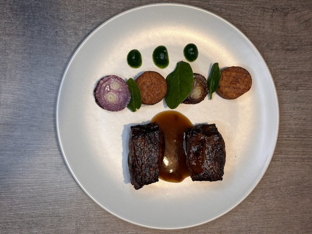 Plat gourmet avec viande rôtie, sauce, légumes et feuilles vertes sur assiette blanche