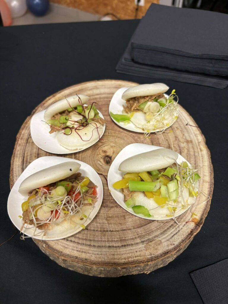 Quatre sandwichs bao aux légumes et viande présentés sur une tranche de bois