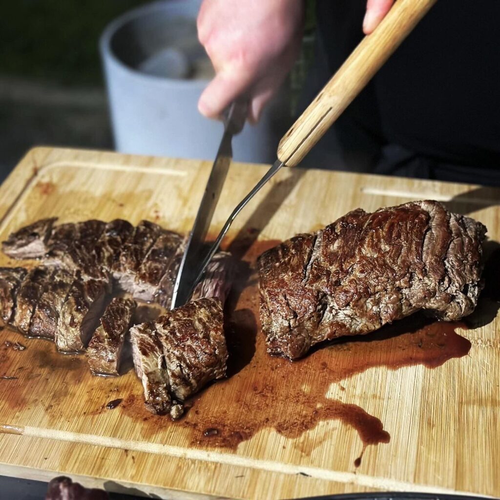 Viande cuite tranchée sur une planche en bois avec couteau et fourchette