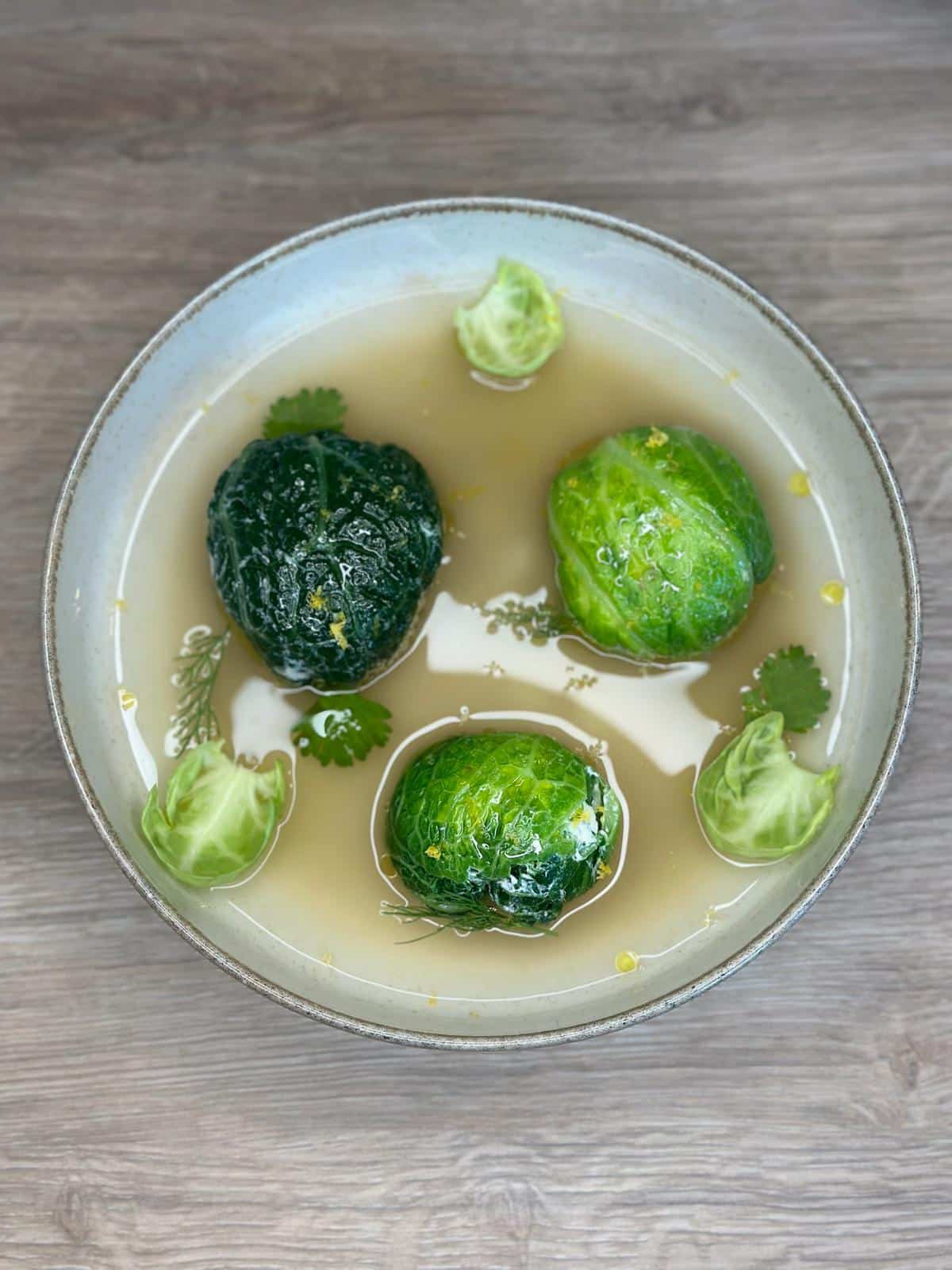 Soupe claire avec choux de Bruxelles et herbes dans un bol blanc sur table en bois