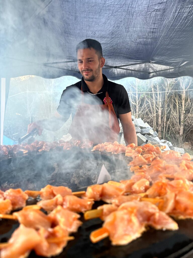 Homme cuisant des brochettes de viande sur un barbecue en plein air sous un abri
