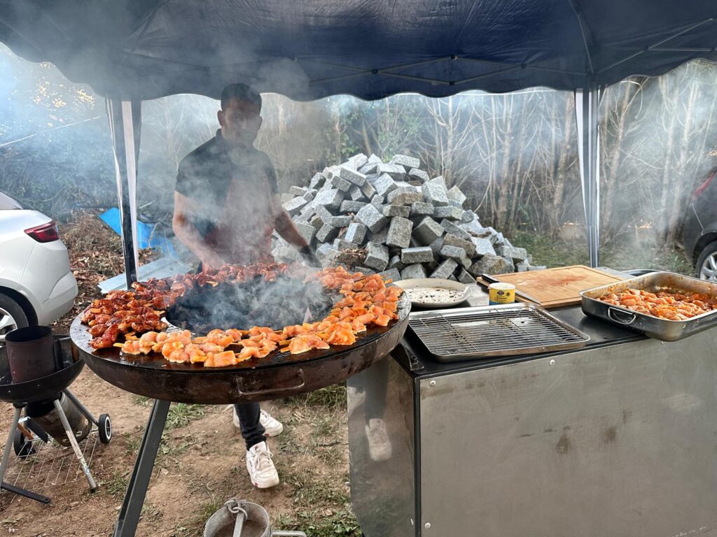 Homme cuisant des brochettes sur un gril circulaire fumant en extérieur sous un barnum