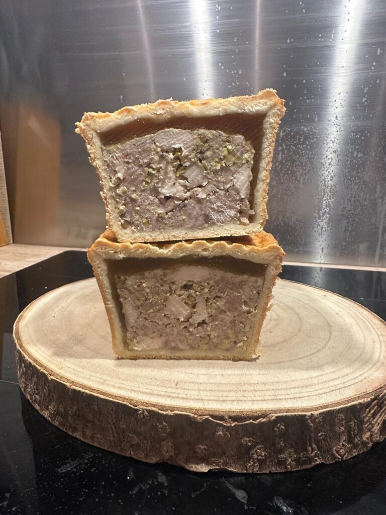 Deux parts de pâté en croûte sur une planche en bois, détaillant la farce et la croûte dorée